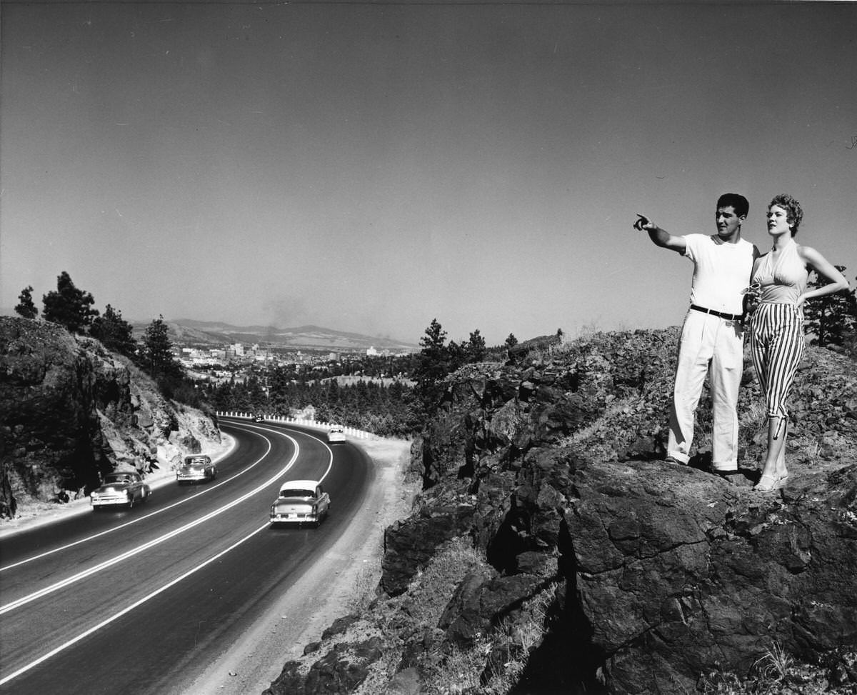 A man and woman standing on a rock formation above a highway, 1940s.