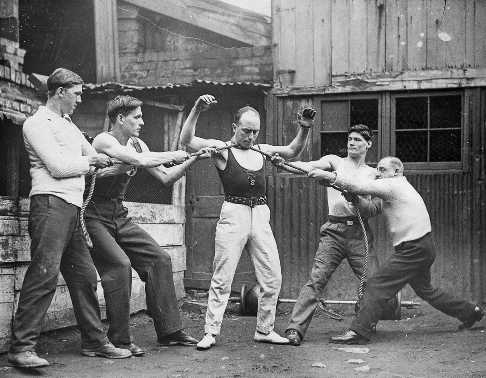 Tom Joyce, who claimed to be the strongest man in Bristol, shows his strength by having four men pull at a rope tied around his neck, 1932