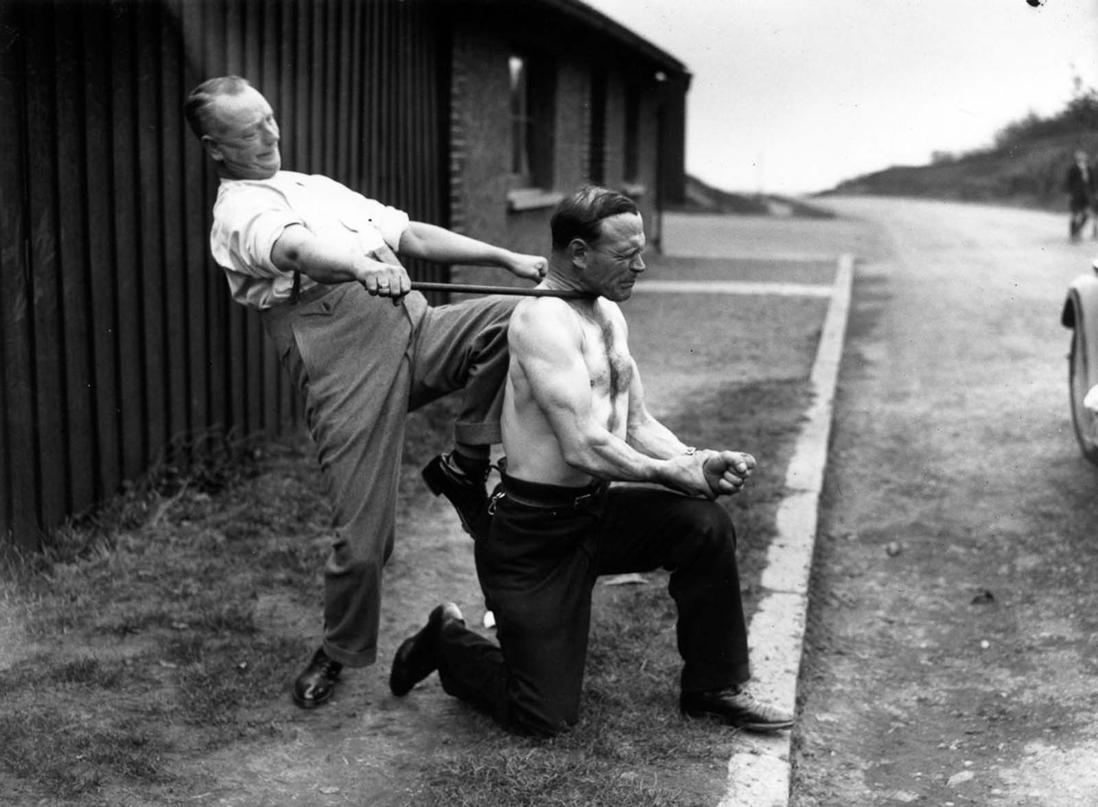 London strongman George Challard allows a companion to bend a piece of iron around his neck, 1935.