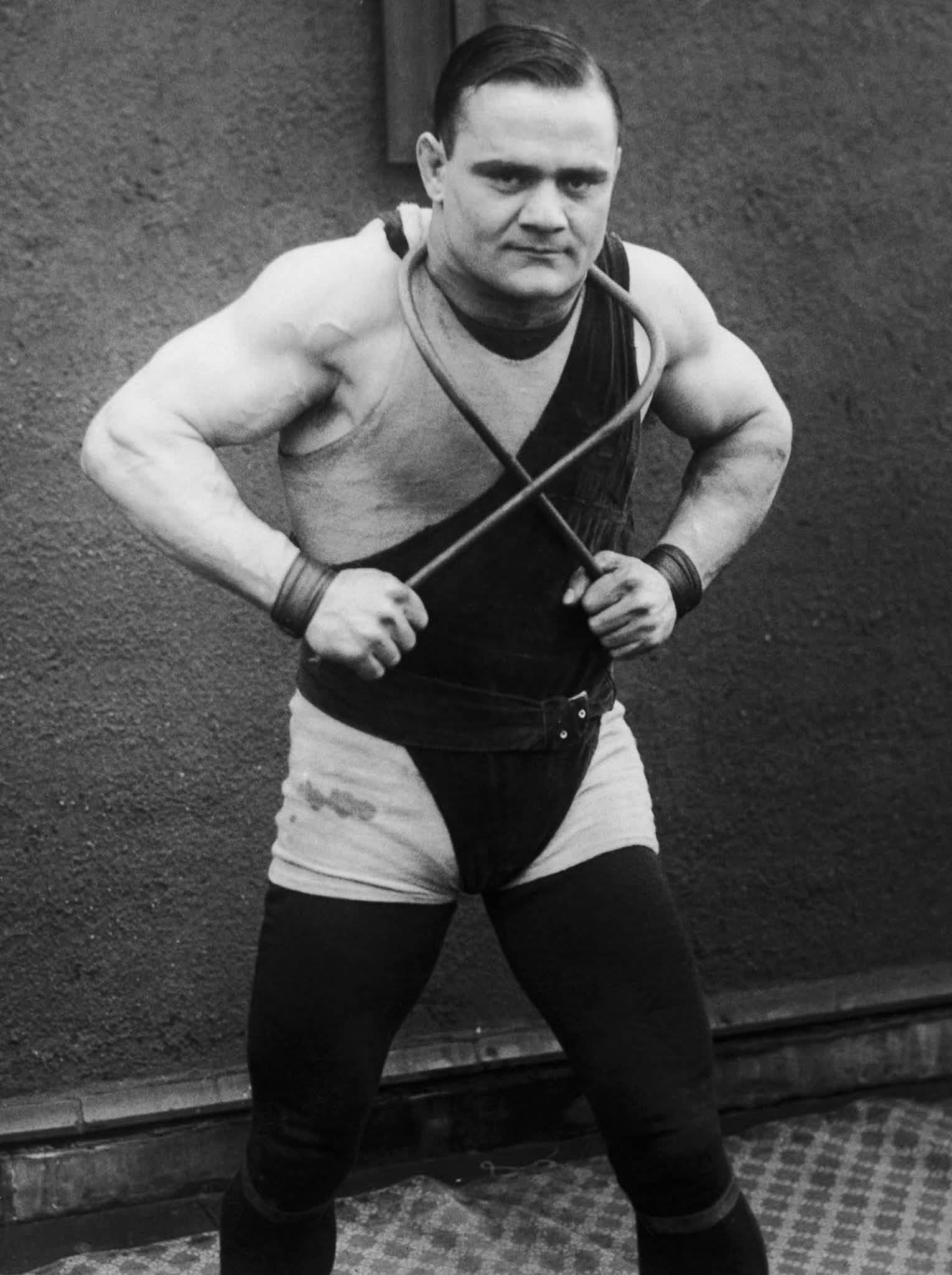 Greek boxer and strongman Just Lessis demonstrating his prowess by bending an iron bar around his neck, 1925.