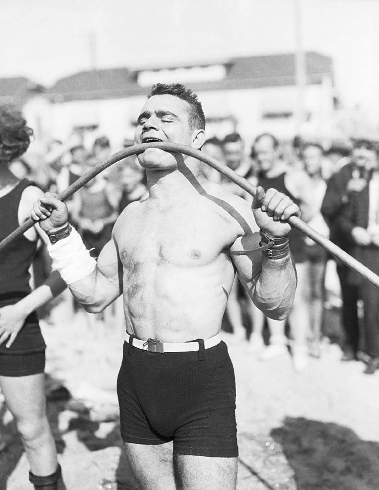 Strongman Gus Lasser bends an iron pipe with his mouth, 1920s.