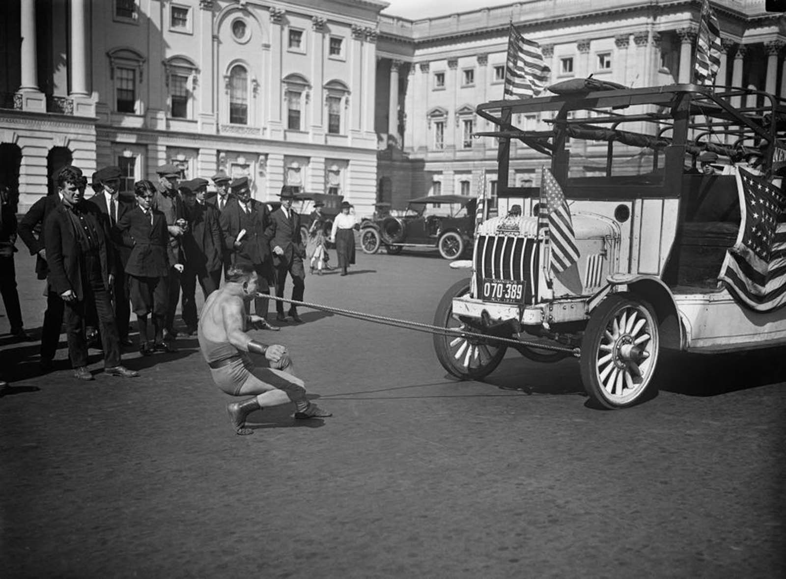 A strongman pulls a car with his teeth outside of the U.S. Capitol building in Washington D.C., 1921