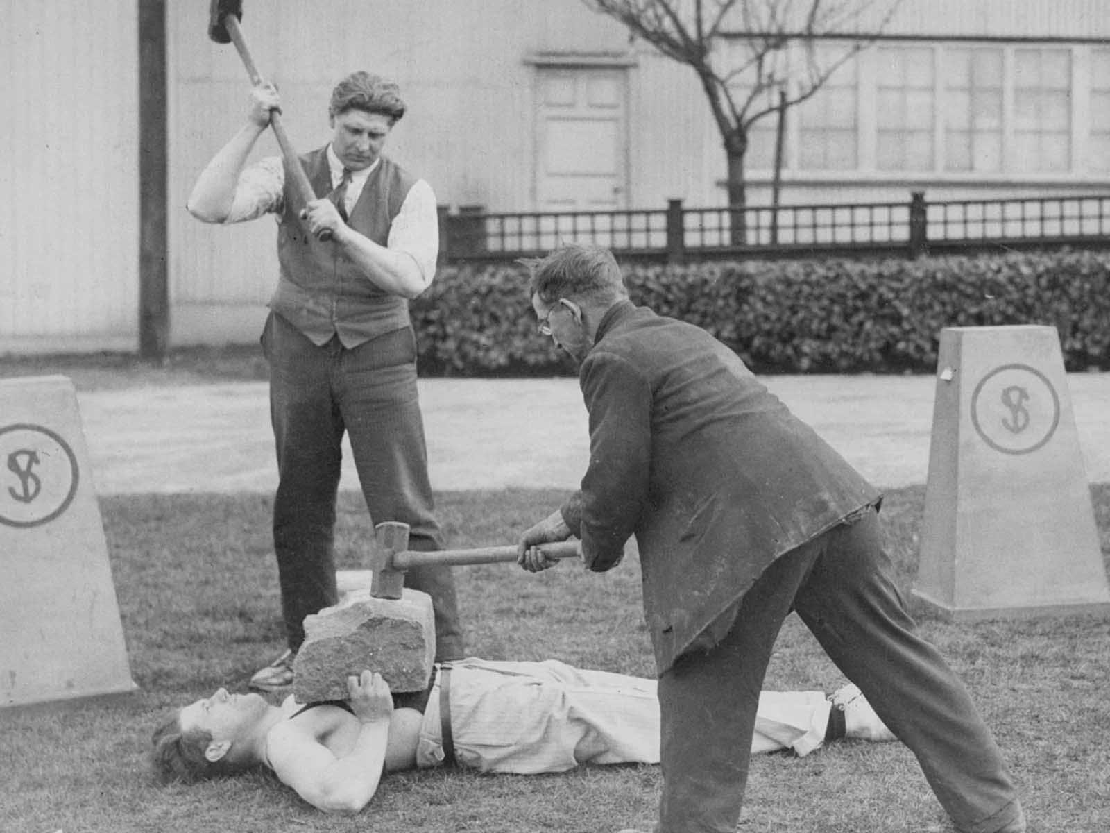 A strongman holds a rock on his chest while two men try to smash it with hammers, 1945