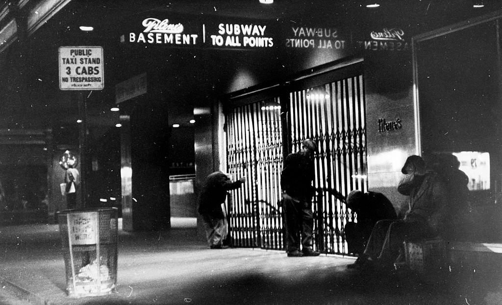 Homeless people stand around a closed entrance to a subway station under Filene's Basement in Downtown Crossing in Boston at night, September 1962.