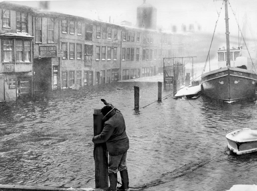 A fisherman secures a boat at T Wharf in Boston as tidal waters flood nearby houses on Jan. 20, 1961.