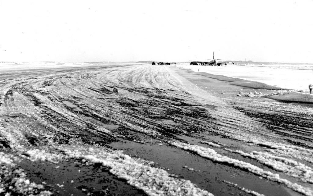 A snowy runway that a jetliner veered off of at Logan Airport in Boston on Dec. 17, 1960, as emergency crews work to shovel the plane out of the snow in background.