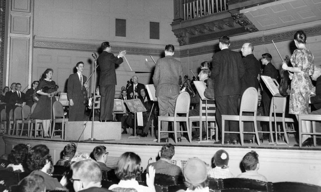 Conductor Harry Ellis Dickson of the Boston Symphony Orchestra applauds Massachusetts high school students who played alongside members of the world-famed orchestra in Symphony Hall in Boston on March 12, 1960.