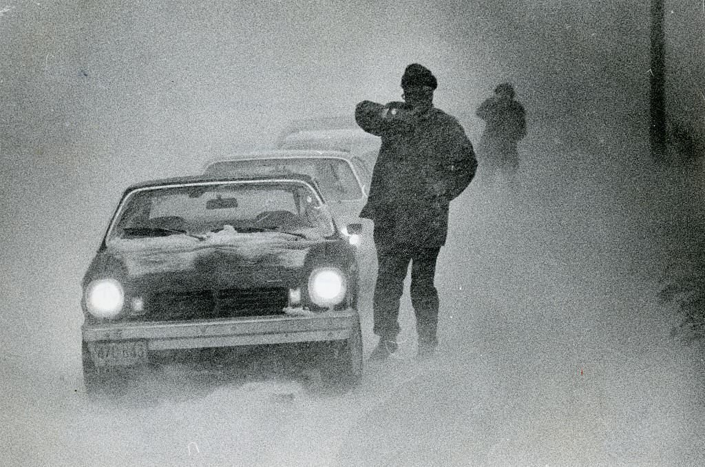 People walk by cars trying to make it through the heavy snow and low visibility on Feb. 6, 1978.