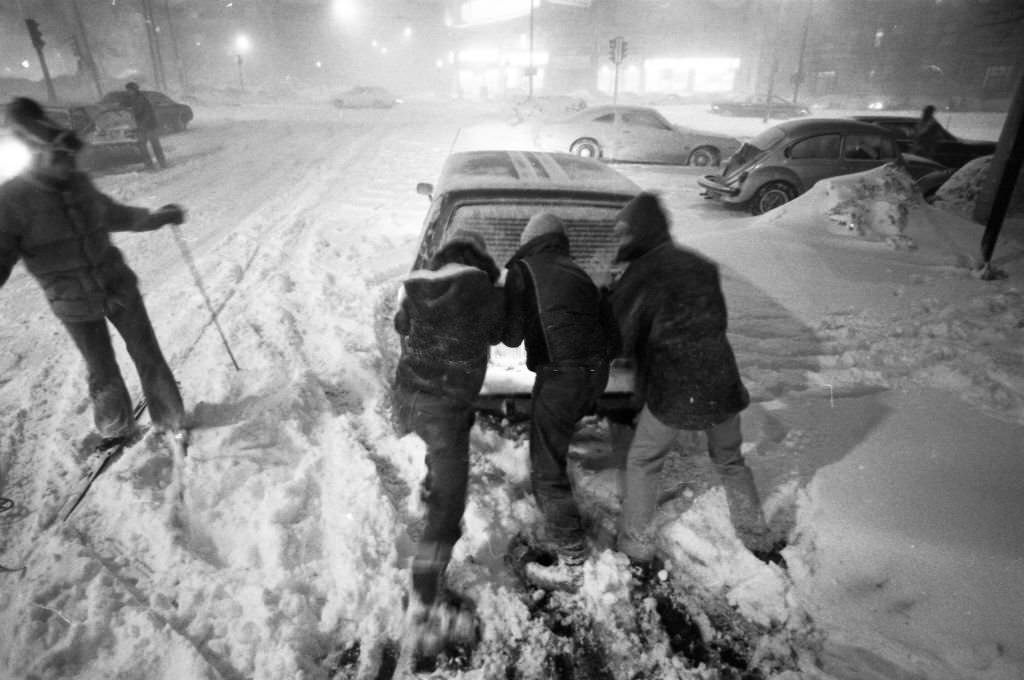 Three people push a disabled car as a skier passes on Kelton Street near Commonwealth Avenue in Boston on Feb. 6, 1978.