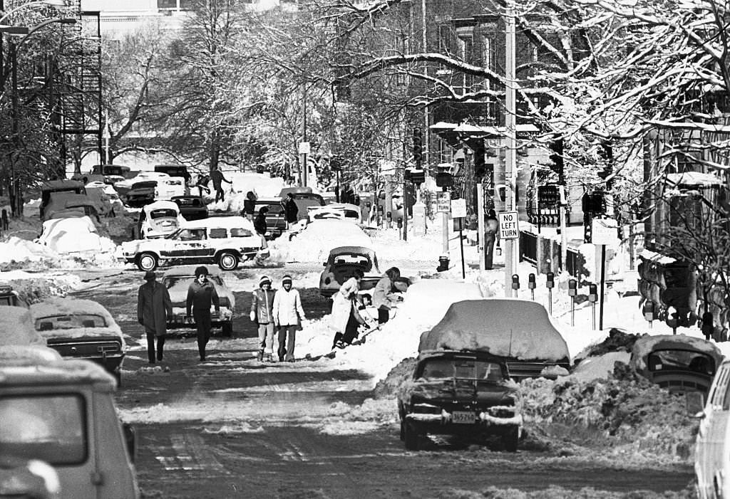 People shovel and walk along, trying to get their cars out of the snow on Hereford Street in Boston's Back Bay, 1977.