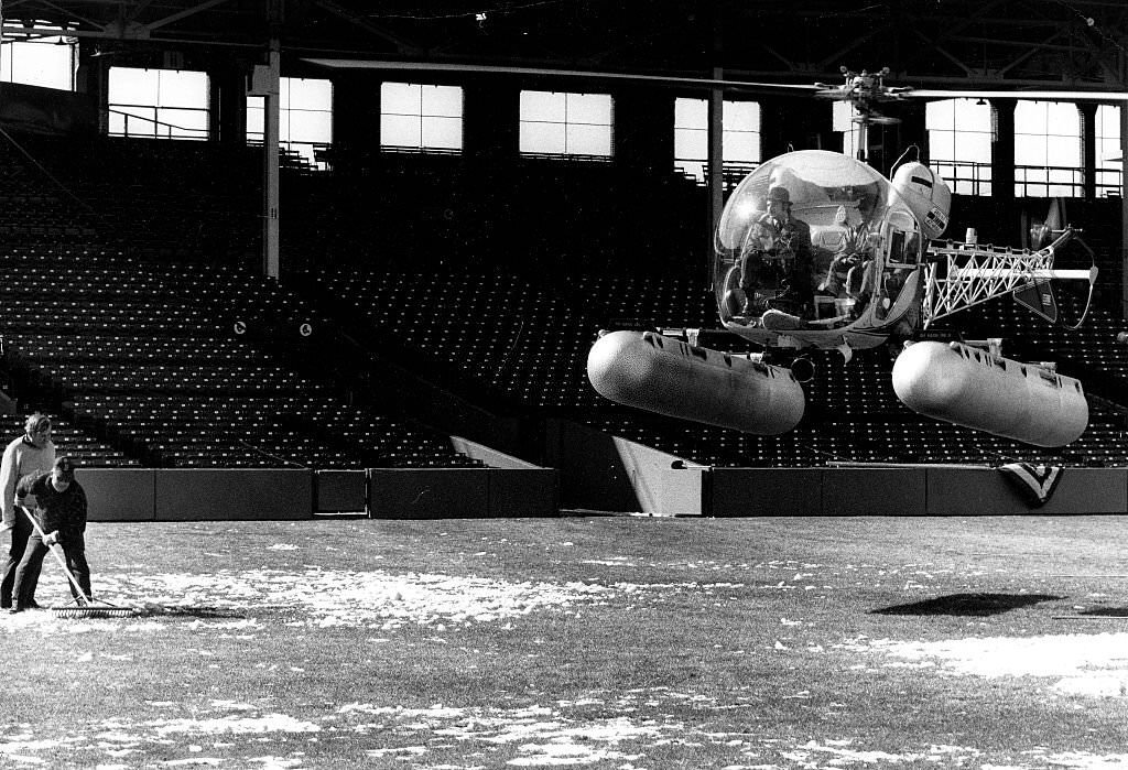 Ground crew members at Fenway Park get assistance from the blades of a helicopter.
