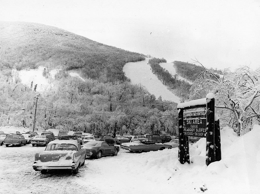 Snow-covered cars are parked at the base of a snowy Cannon Mountain in Franconia Notch State Park in Franconia Notch, 1969.