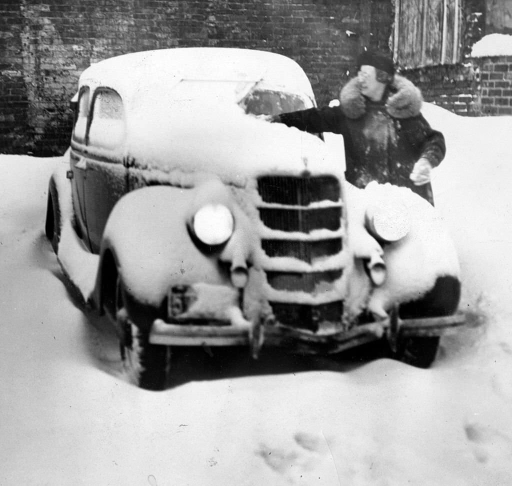 Mrs. Patricia Mortimore, of Brookline, Mass., cleans snow off windshield to start home, 1936.