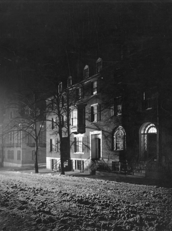 Night winter view of snowy Chestnut Street, a few rowhouses lit from within, Boston, Massachusetts, 1906.