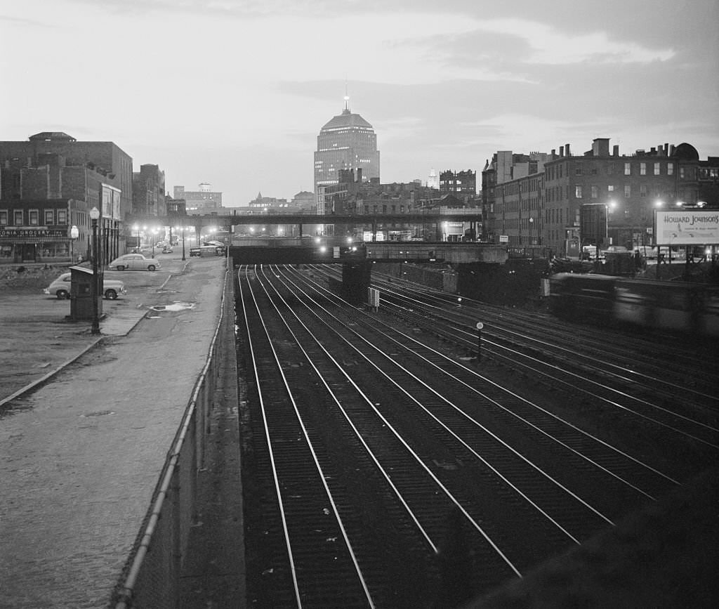 As the sun sets in Boston, railroad tracks reflect the fading light and lead the eye along to the John Hancock building, which dominates the skyline in skyscraper scarce hub city.