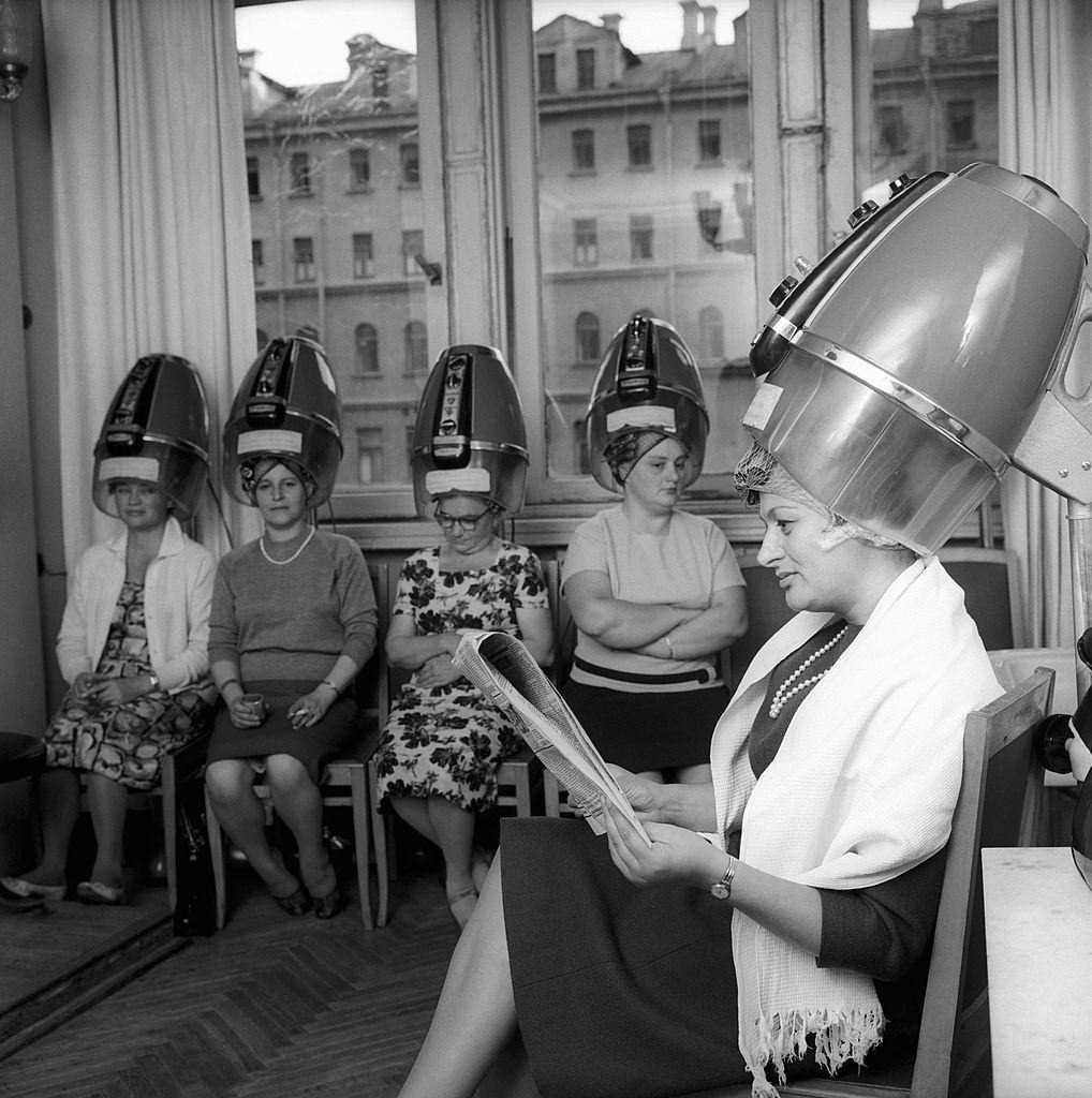 Edda Vincenzi at the hairdresser's; she is sat down and is reading a Russian newspaper. Moscow, September 1964.