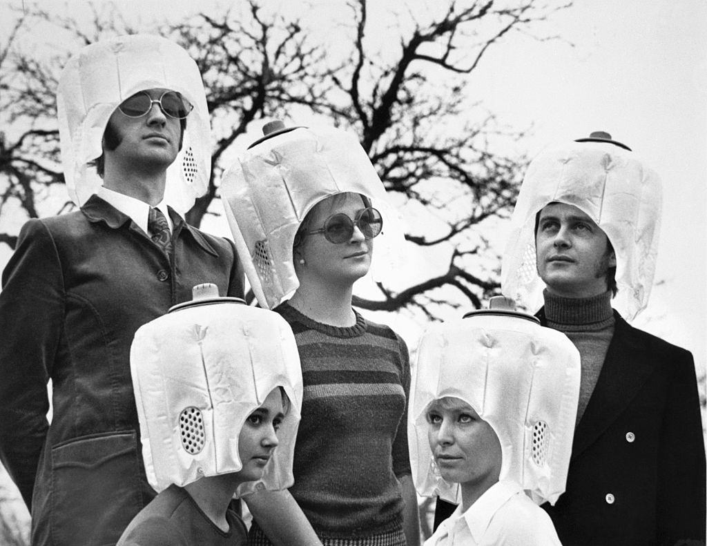 A group of men and women wearing the "Lady Braun" hover hood hair drying device, 1960s
