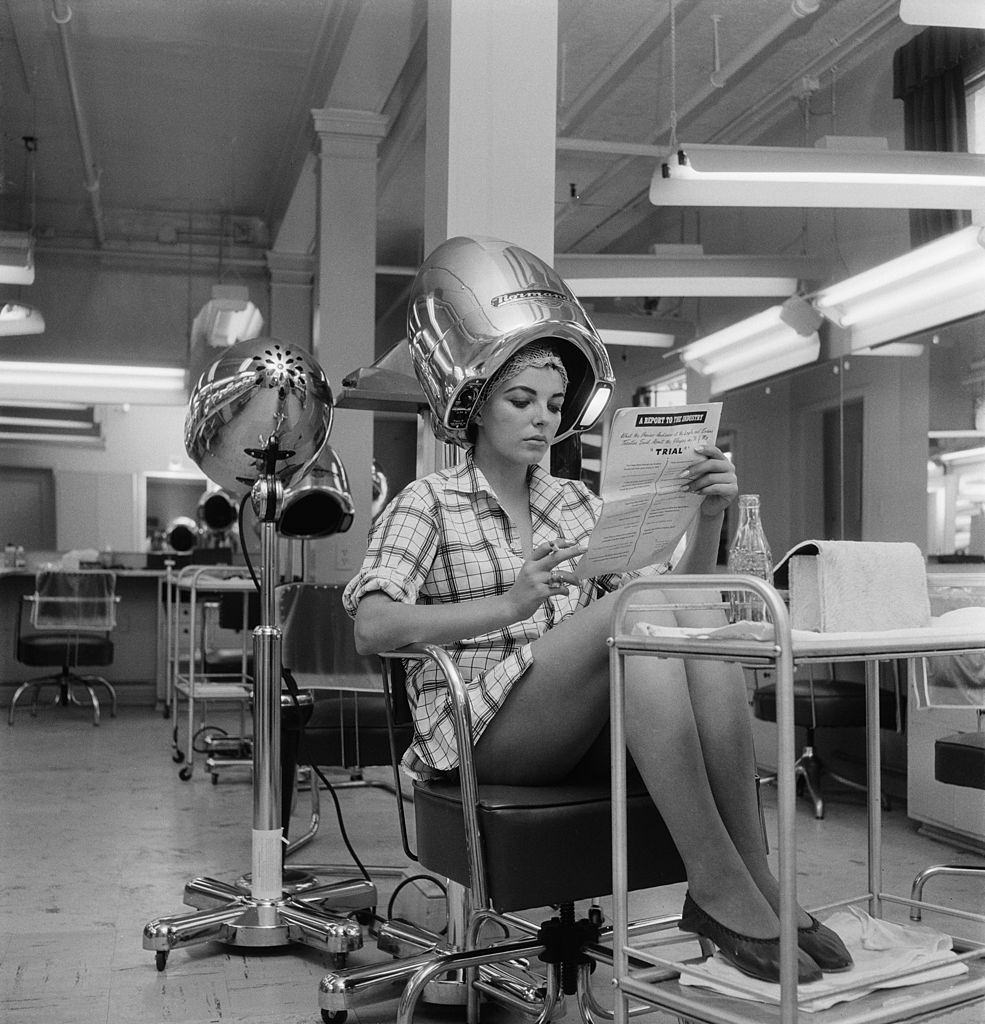 English actress Joan Collins waits for her hair to dry in a film studio, 15th August 1955.