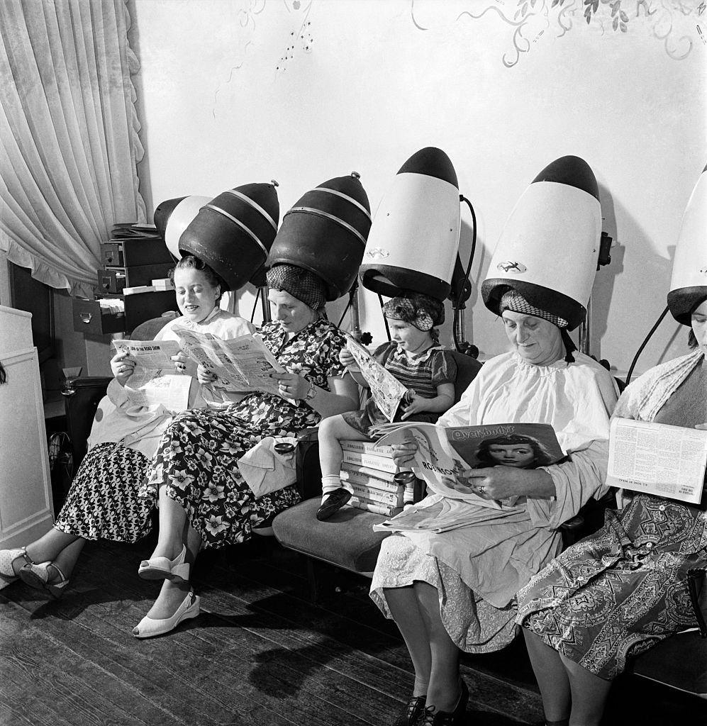 Old women sitting with their heads under a dryer as they get their hair styled, 1953s