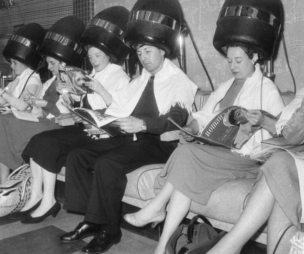 A man surrounded by women under the hairdryers at a new unisex hairdresser's, 1950s