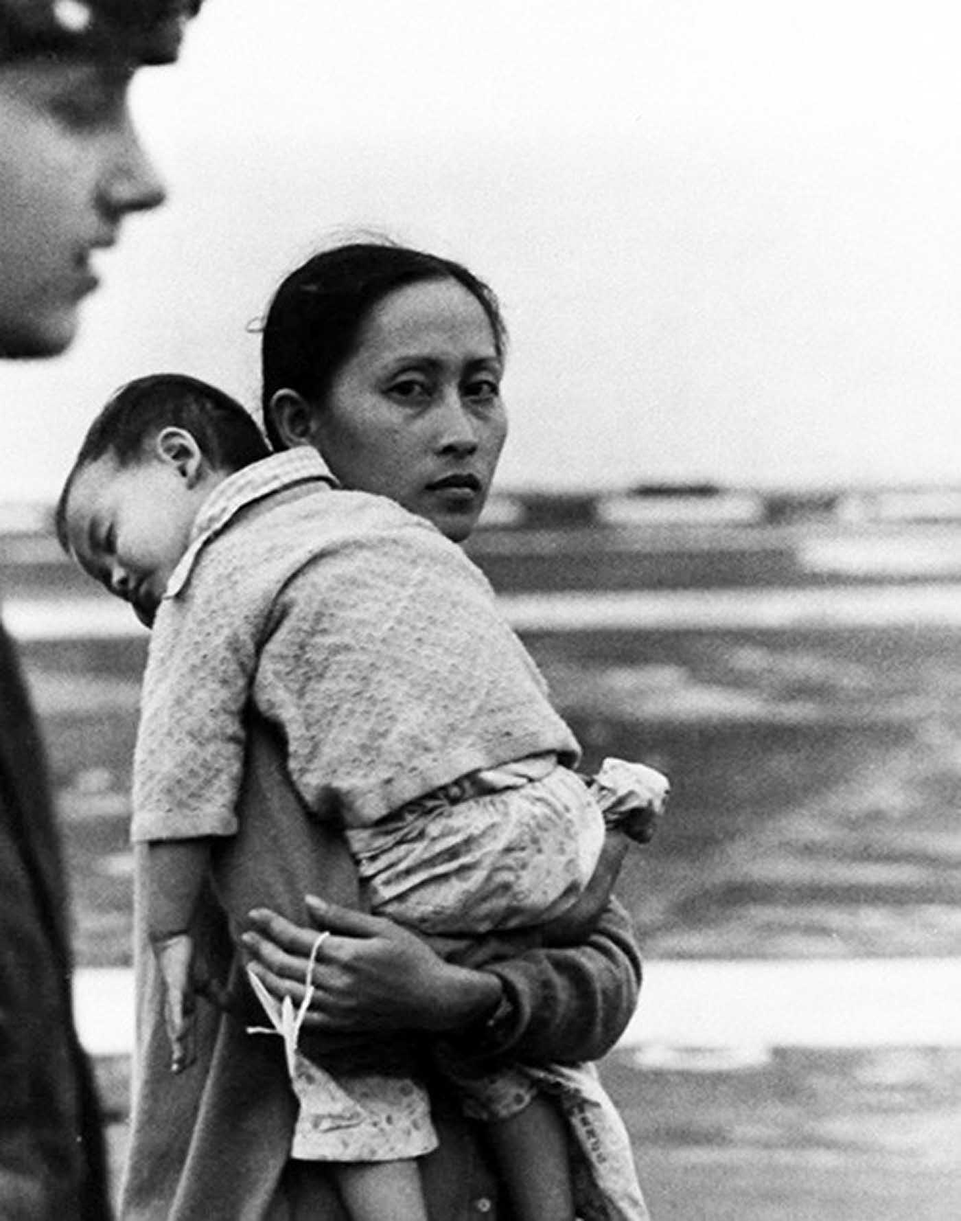 A Vietnamese woman, carrying her son, is given a numbered tag as she arrives onboard USS Hancock (CV-19).
