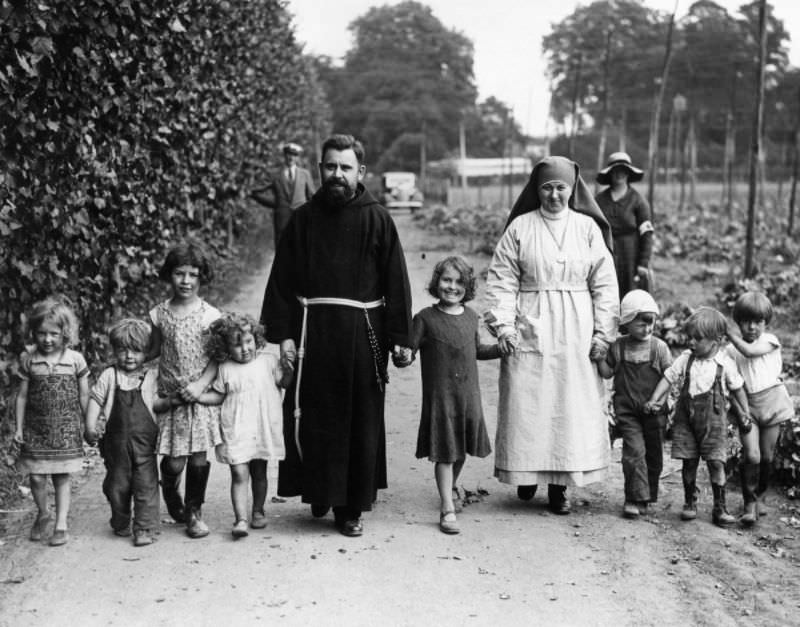 A Franciscan friar and nun walk with hop pickers' children at Paddock Wood, Kent, 1934.