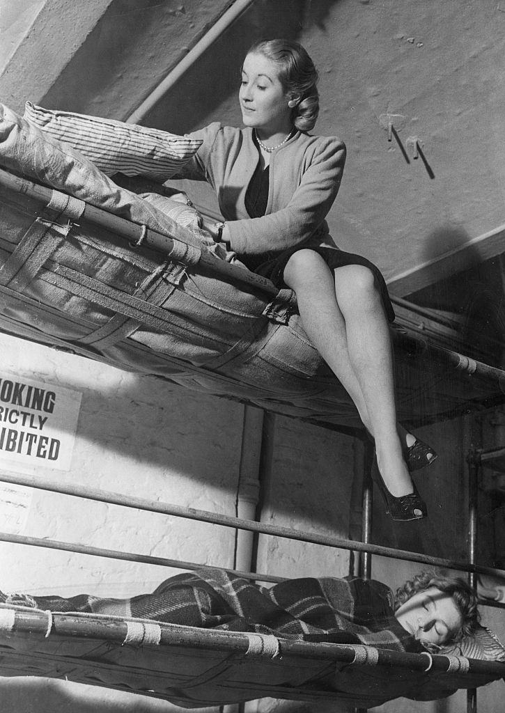 A woman fixes her matress and pillows on the top bunk of her bed as she prepares for a nights sleep in an air raid shelt