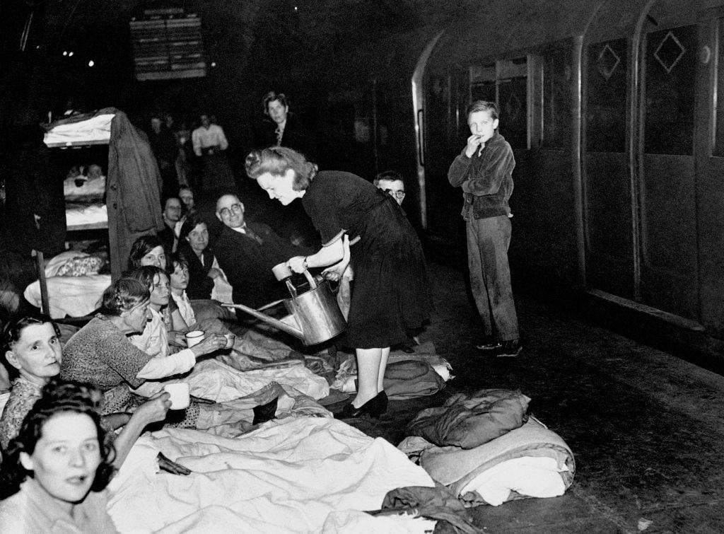 A woman dispenses water from a watering can as Londoners take shelter in the London Underground during the Blitz.