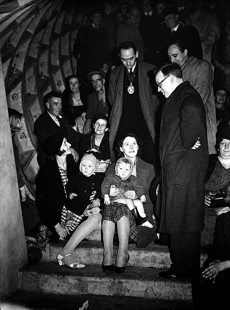 Cabinet Minister Herbert Morrison chatting to women and children on the stairs of a London tube station where they are sheltering from air raids, 1940