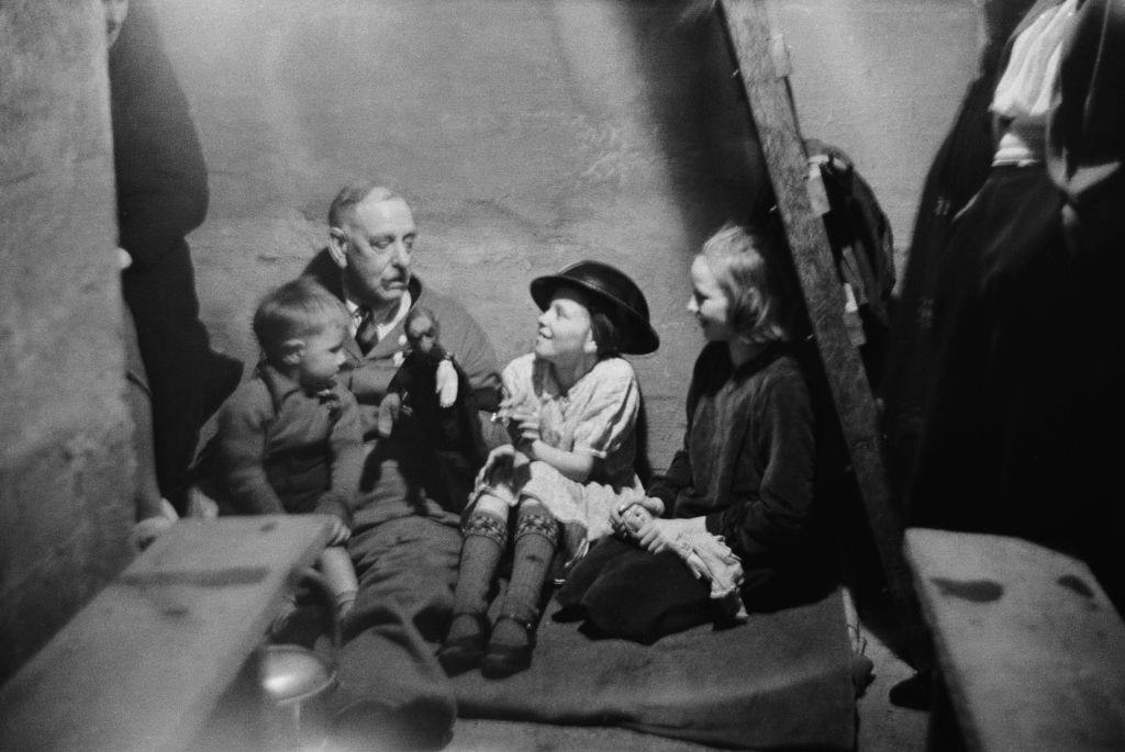 A man entertaining three children with a toy in an air raid shelter during the Blitz, London, October 1940.