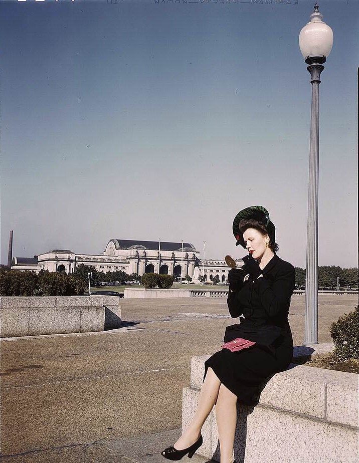 Woman putting on her lipstick in a park with Union Station behind her, Washington, D.C., 1950s