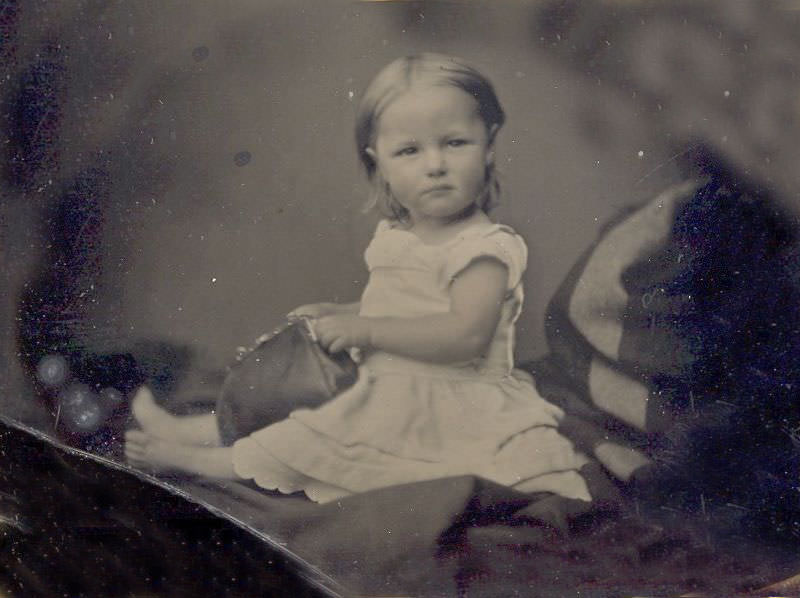 Cute little girl most likely sitting on mom's lap (hidden under blanket) while playing with her mother's purse