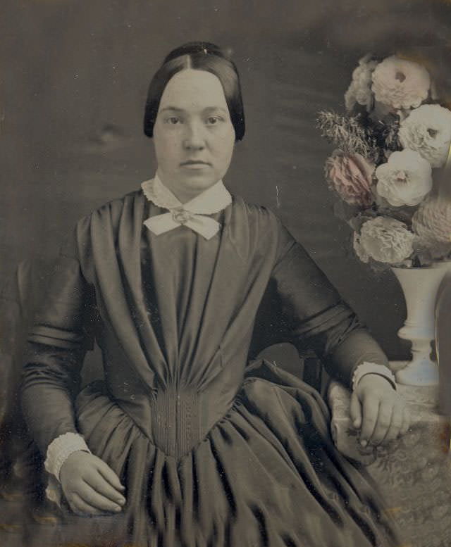 A woman posed by a vase of flowers