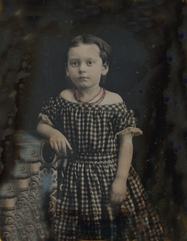 A darling little girl in a tinted off shoulder dress and red coral necklace