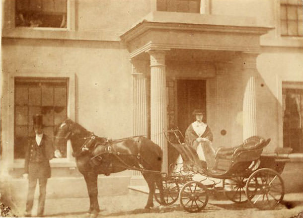 Man, woman and horse-drawn carriage before a colonnaded porch