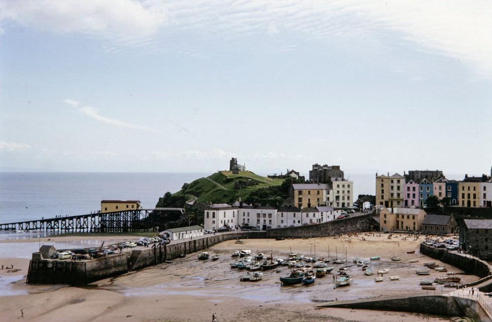 Tenby Harbour, Tenby, Pembrokeshire, Wales, 1964. Tenby Harbour at low tide, in which boats are beached, with Castle Hill and colourfully painted houses on Bridge Street and Pier Hill.