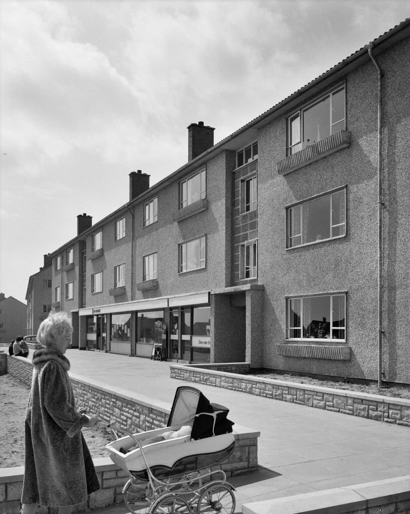 A view of a block of Easiform flats with a ground floor shop in Chepstow, showing a woman pushing a pram in the foreground.