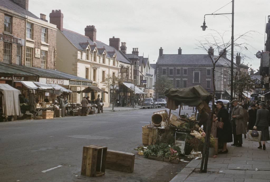 Pedestrians and shoppers buy produce from market stalls lining a main street in the centre of the town of Mold in Flintshire, Wales 1960.