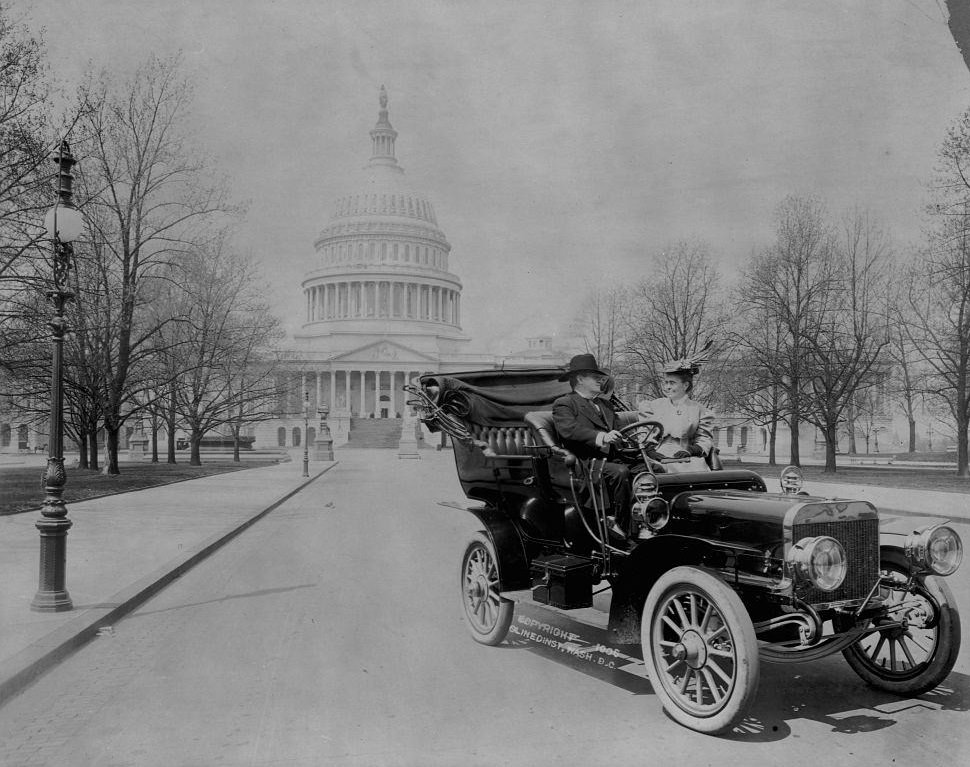 Senator Benjamin Ryan Tillman seated in an automobile with a woman in front of the U.S. Capitol building.