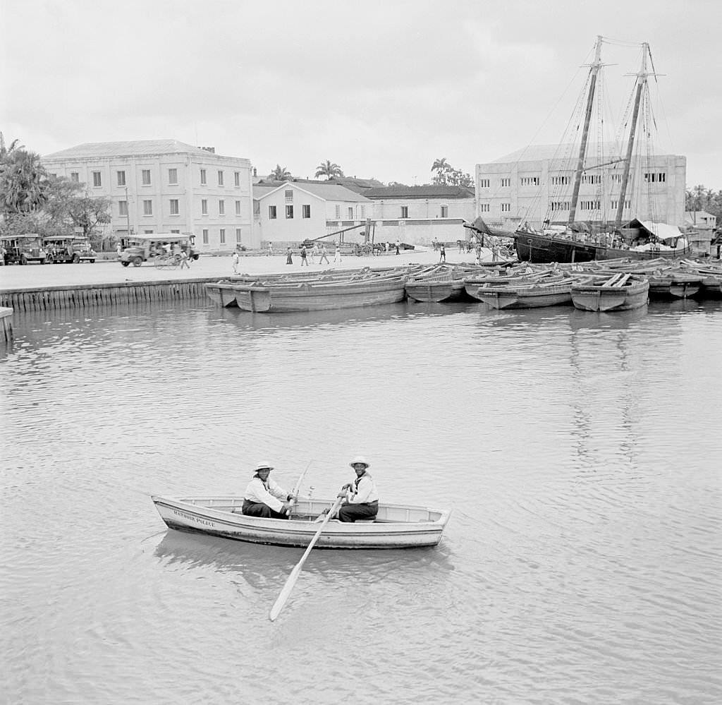 Two local men row a boat in the harbor in Bridgetown, 1946