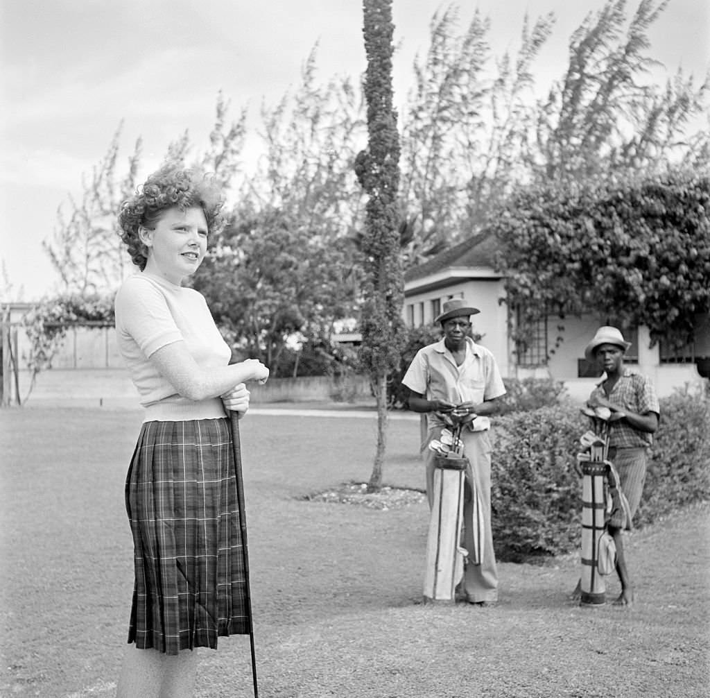 A women looks to play golf as two local men caddie in Bridgetown, 1940s