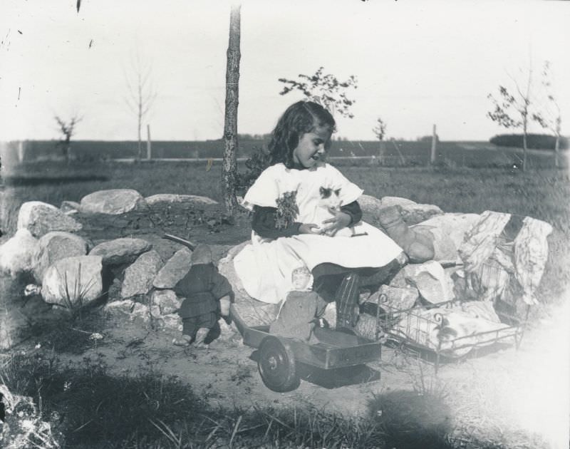 Little girl playing with a kitten and dolls, 1900s
