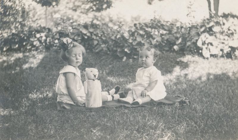 Two little girls sit on the grass with a stuffed toy, 1920s