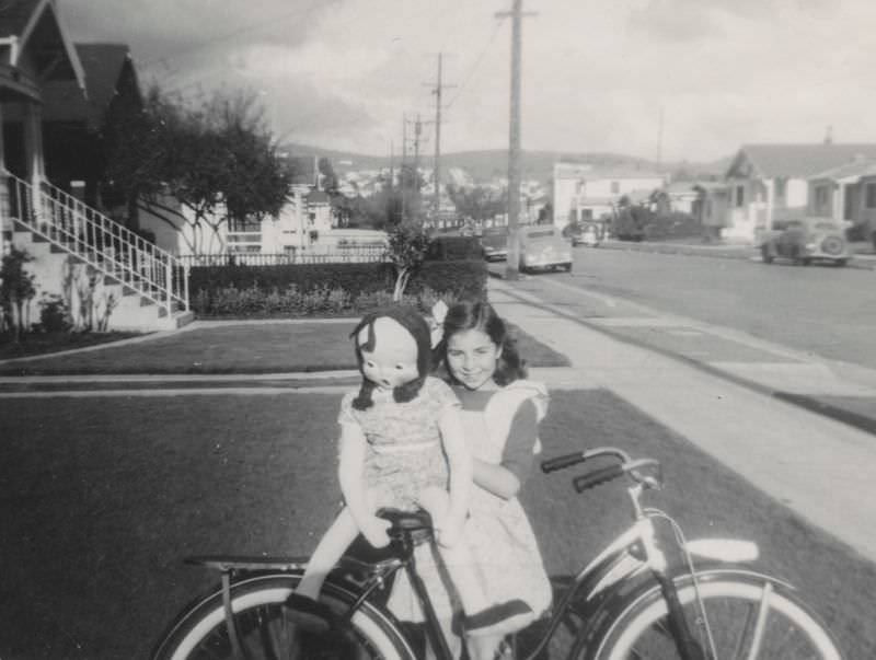 Little girl poses with her doll and bicycle, 1940s