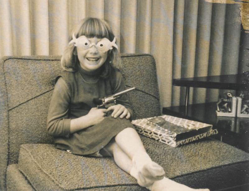 Little girl carrying a toy gun and wearing goofy glasses, December 1964