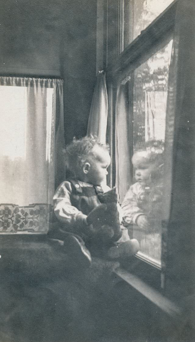 Baby looks out of a window while holding a teddy bear