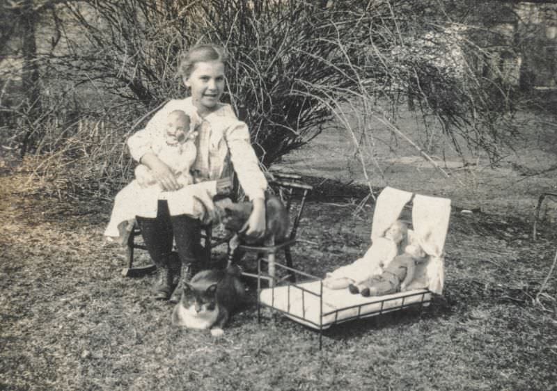 Little girl sits with her dolls and cats, 1910s