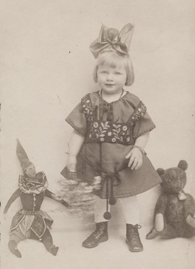 Little girl poses with her teddy bear and stuffed joker, 1920s