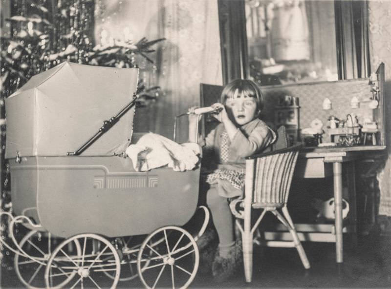 Little girl sits with a doll house and baby carriage, 1920s