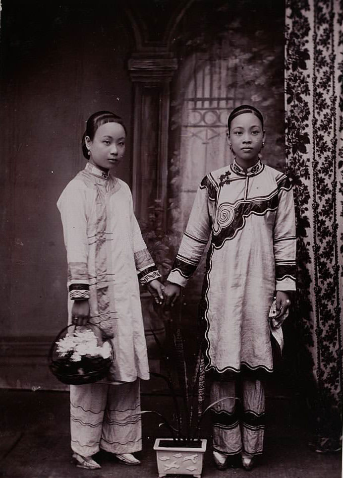 Two young Chinese women in silk tunics and pants. Both have bound feet, 1900s